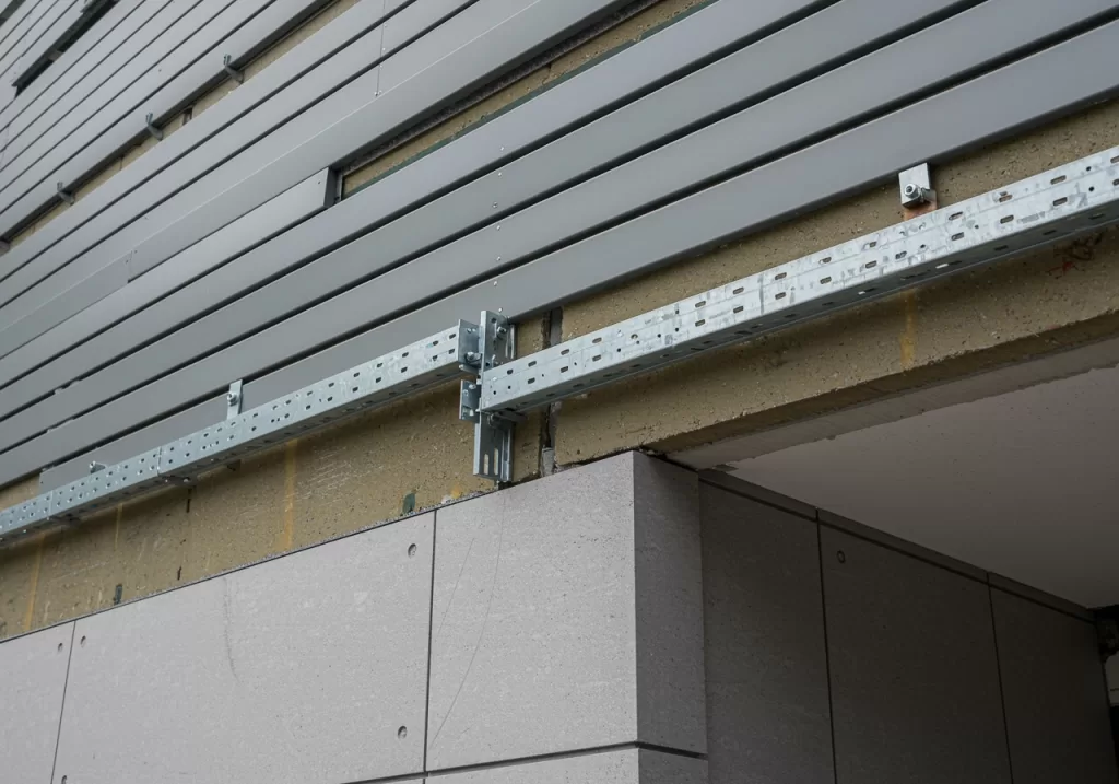 Façade de bâtiment en cours d’installation avec accessoires métalliques pliés sur mesure, incluant couvertines, bavettes, solins et profilés assurant l’étanchéité et la finition.